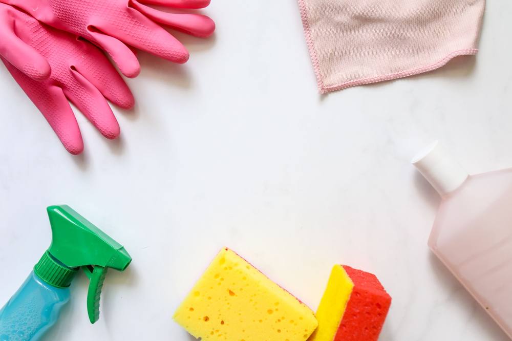 Flat lay of cleaning supplies: gloves, cloths, sponges, and spray bottle